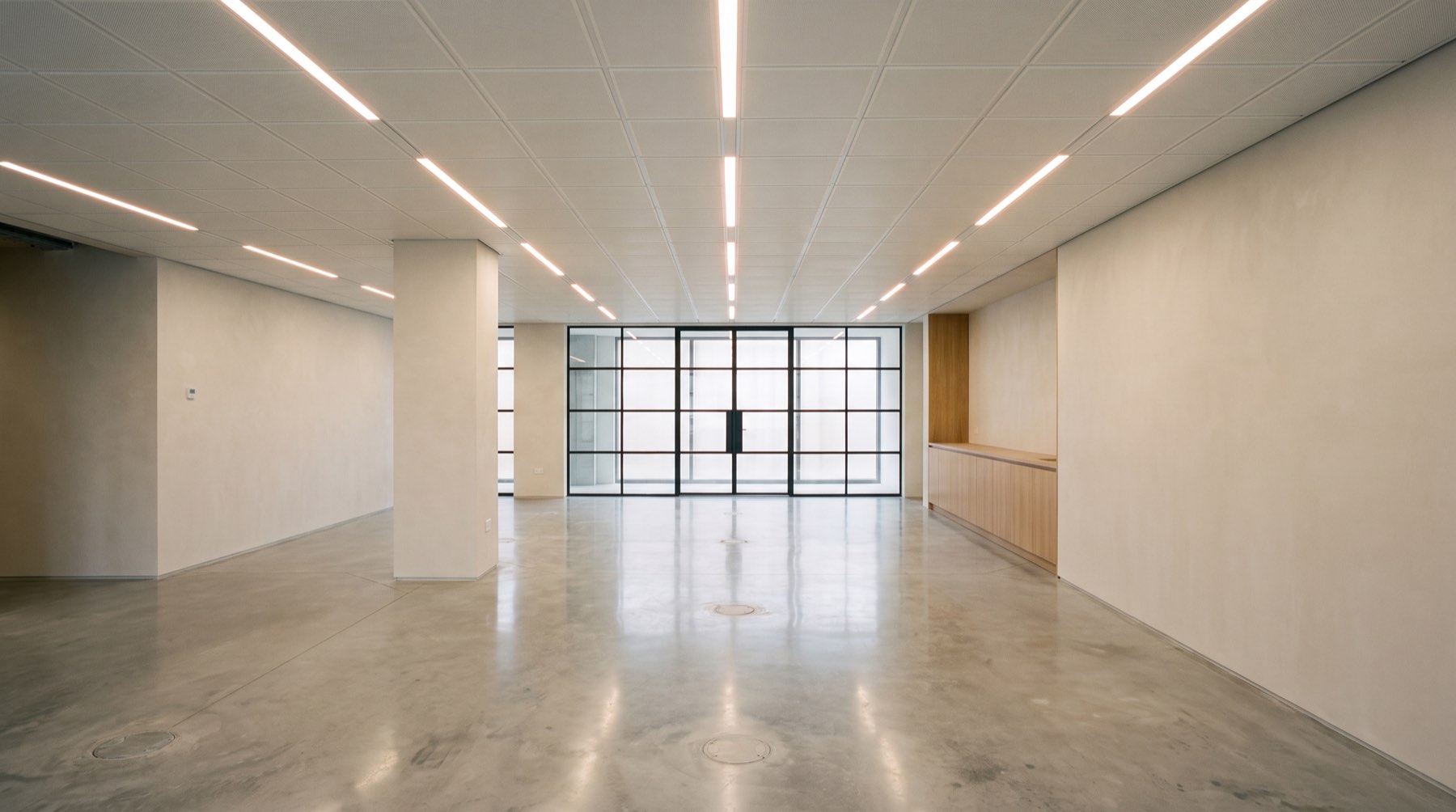 The same frame finished: ceiling grid in, linear luminaires lit along every second line, floor polished